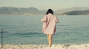 Slow motion video of a girl going swimming in the sea and taking off her clothes. Beautiful woman takes off her shirt to swim in the ocean on vacation.