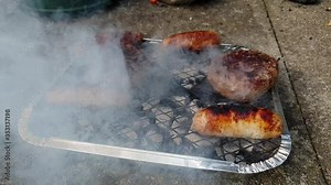 Burgers and sausages cooking and smokoing on a disposable barbecue