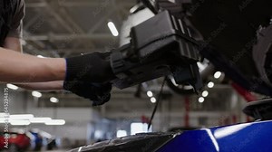A male car mechanic removes plastic protection from a car engine at a service station