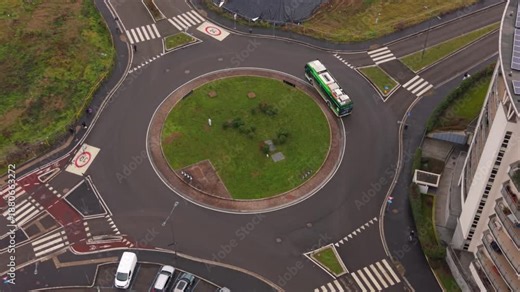 Aerial View of Roundabout: An eye-level shot captures a roundabout with a bus entering the circulation and several vehicles parked, showing a typical urban landscape and infrastructure.