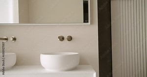 Modern bathroom with minimalist interior, ceramic washbowl, chrome water tap and mirror. Wall mounted faucet with concealed system. Contemporary clean public lavatory with wash basins
