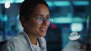 Portrait of Beautiful Black Latin Woman Computer Screen Reflecting in Her Glasses. Young Intelligent Female Scientist Working in Laboratory. Background Bokeh Blue with High-Tech Technological Lights