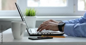 man typing on laptop keyboard working in white bright office
