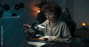 A boy is sitting at a desk in front of a soldering iron. He is repairing computer hardware engineering, technology, science, concept. A child is soldering an electronic component.