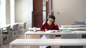 Smart asian girl reading textbook and taking notes writing outline while preparing for exam, sitting in empty quiet university reading room or library, korean female student learning in classroom