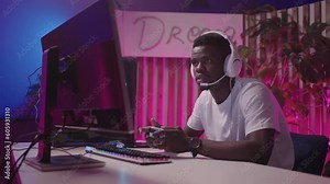 Immersed in the Cyberworld: African American Man Playing Video Game on His PC with Joystick and Headset, Socializing with Playmates
