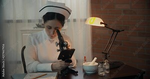 A wider view of a 1930s era nurse using a microscope who takes notes on her findings. Color version Stock Video