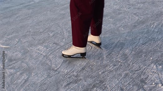 Close-up of woman ice skating on frozen lakewhite figure skates on frozen ice rink surface with scratch marks and patterns from skating blades
