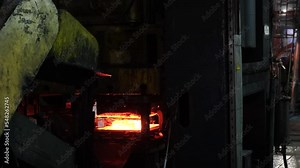 caucasian young strong blacksmith working with open fire in furnace. The blacksmith forging hot iron workshop.Red hot steel metal billets after molten steel casting. Continuous casting machine