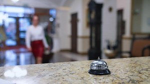Reception lobby. Bell button on a reception table on blur background of a hotel. Lady pressing the metal bell on desk to call a receptionist in hotel. Close-up.