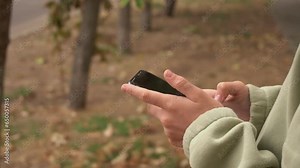 A child uses a smartphone on the street, pressing with a finger, plays, reads, communicates. Mobile phone in two hands.