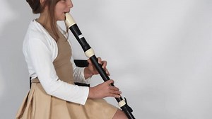 Girl playing, practicing the flute, playing a melody on a musical instrument, wooden pipe, sitting on black chair on white background. Out-of-school children activities, lessons