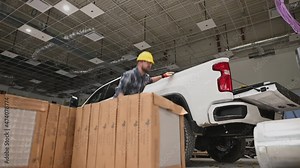Construction Worker in Yellow Hard Hat Jumping Out of His Pickup Truck Bed While Working Inside a Warehouse.