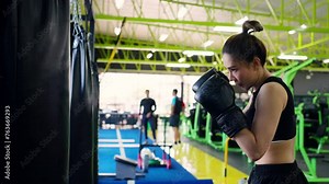 4K Confidence Asian woman athlete in sportswear with boxing gloves do workout exercise punching boxing bag at fitness gym. Healthy fit and firm woman do sport training and bodybuilding at sport club.