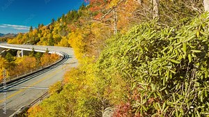 A Scenic View Panning Towards Linn Cove Viaduct against Grandfather Mountain on the Blue Ridge Parkway near Linville NC with Fall Colored Trees and the Layered Smoky Mountains topped by a Blue Sky