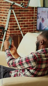 Happy gamer playing spaceship flying game on smartphone, using gyroscope function. Excited relaxed man being competitive while having fun in nice cozy apartment living room