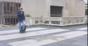 Two mature African American men walking plaza pulling suitcase and checking phones past balustrade