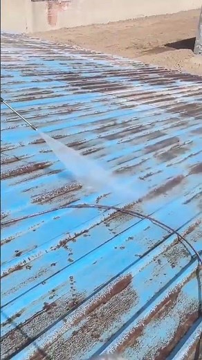 Cleaning a blue corrugated metal roof using a high pressure water sprayer