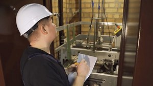 Elevator maintenance. Repair of elevator equipment. Elevator emergency stop. A close-up worker near the elevator car shaft records and measures the elevator's performance readings.