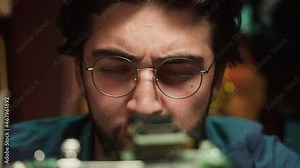 Concentrated hacker looking at microchip close-up. Young Spanish man developing program. Professional programmer working with microprocessor. Assembly of computer equipment, repair service.