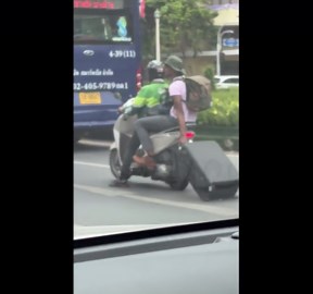 Tourist carries suitcase along road by dragging it behind motorcycle