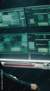 Concept shot of cyber criminal taking seat at table and starting to write malicious program on computer, in dark room for massive attack of corporate big data servers. Vertical shot.