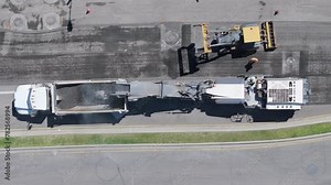 Overhead view of a busy road construction site with asphalt paving machinery, workers, and a queue of trucks. Footage 4K.