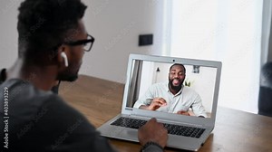 Back view African-American men talking online via video call, multiracial employees have video meeting. Two biracial guys using laptop for virtual conversation