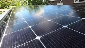 Solar panels in an array on flat rooftop, house and trees in background