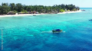 Boats sailing in the perfectly clear sea surrounding tropical island with trees and white sand beach in Bermuda islands.