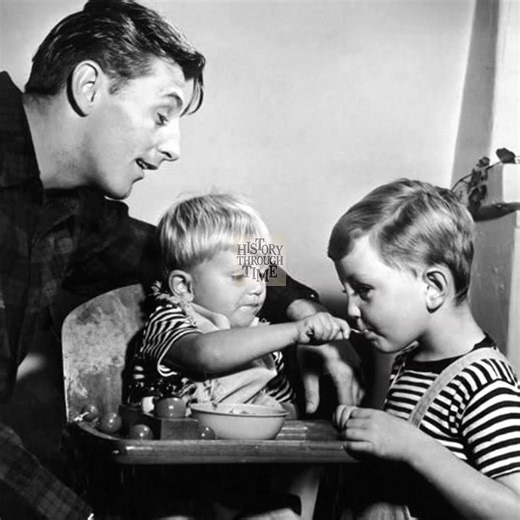 "Robert Mitchum and his wife, Dorothy, enjoy a serene afternoon at their California home in 1949, joined by their young sons, James and Christopher. At this point in his career, Mitchum was already a celebrated star, known for his charismatic performances in film noir classics and Westerns. Away from Hollywood sets, the couple embraced a quiet, family-centered life, with their home becoming a haven from the industry’s constant demands. This rare glimpse into their personal world captures the war