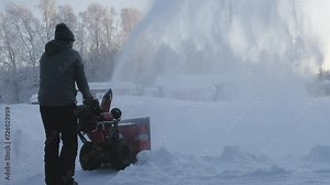 Much snow blowing from snow blowing machine, rear view video on man working outside, removing much snow after recent snowfall. Frosty air.