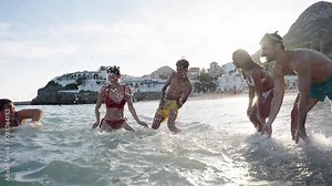 A group of young friends in swimwear having fun splashing water on each other on the shore of the beach. Diverse people playing water games of the Gen z playful during the summer holidays