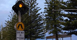 A pedestrian crossing sign with flashing yellow lights warns drivers to give way to people in Australia. Concept of road priority and traffic safety.