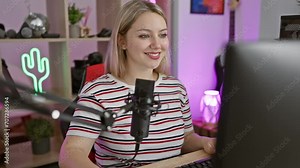 Cool and confident, young blonde woman streamer smiling with perfect teeth, laughing and playing video game on computer in dark gaming room at night