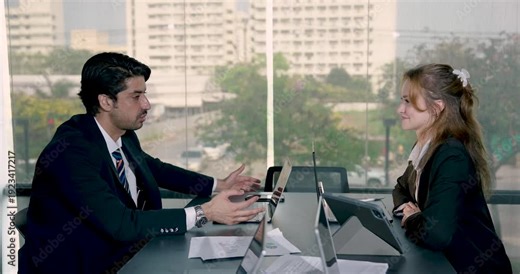Smiling businessman engaging in lively business conversation with female colleague in office. Friendly multicultural interaction highlighting teamwork and business strategy discussion