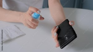 Slow motion: woman spraying antiseptic and cleaning black smartphone with disinfectant wet wipe. Disinfection, protection, prevention, COVID 19, coronavirus, safety, sanitation, technology concept