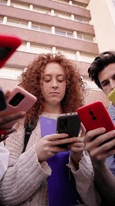 Vertical low angle. Group of young serious people in circle using cell phones together. Concentrated friends gathered looking mobile screen watching content on social media. Gen Z technology addicted