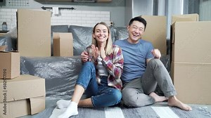 young happy married couple who have just moved to a new apartment talking online on a video call looking at the camera. Webcam view. Mixed race family owners communicate remotely with friends at home