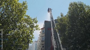 Back view of firefighters in elevated platform extinguish burning house using extended ladder equipped with water hose to spray water onto the building roof with smoke. Fireman extinguishing fire Stock Video