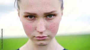 Close up portrait of young teen girl with expressive eyebrows, red cheeks and freckles look at camera and shows emotion sadness.