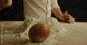 Chef twists egg on table before cracking it in flour, kneading dough for pizza close up, red epic, slow motion, cooking process
