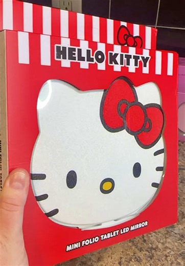 Hello Kitty Folio Tablet LED Mirror, officially licensed Sanrio beauty mirror featuring the iconic Hello Kitty face in a slim, portable folio design. This compact LED makeup mirror includes tri-tone lighting with adjustable brightness, making it perfect for flawless makeup application, skincare routines, and on-the-go touch-ups. Switch between warm, neutral, and cool light to match any environment. Designed with a protective folio cover that folds into a sturdy stand, this Hello Kitty mirror wor