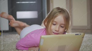 Happy little girl playing with tablet pc computer lying on floor at home.