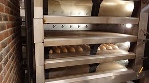 Craft mini-bakery producing French pastries. The baker takes freshly baked hot bread out of the oven. Production of bakery products. Traditional French baguette.