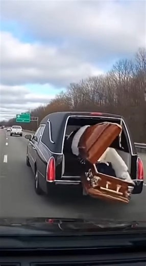 Coffin Tumbles Out of Hearse Onto Highway, Revealing Body Inside A horrifying and unbelievable scene was caught on a dashcam when the rear door of a moving hearse flew open, allowing a casket to slide out onto the busy highway. The footage shows the hearse driving at speed when the coffin spills onto the road, pops open upon impact, and slides down the asphalt, revealing the deceased person dressed in a suit. The driver of the filming vehicle swerved to avoid the grim debris, as a woman immediat