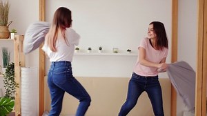 Teen girls fun. Home leisure. Two happy sisters having pillow fight on bed at home.