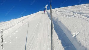 First-Person Perspective: Skiing Uphill on a Button Lift with Skier Ahead Under a Clear Blue Sky