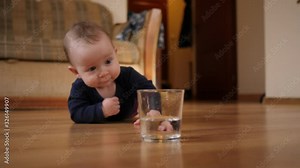 Toddler child awkwardly takes a glass of water and spills water on the floor at home