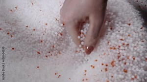A woman mixes plastic granules with orange pigment to create colored plastic. Polymer composites are used in industry as raw materials for the production of various products